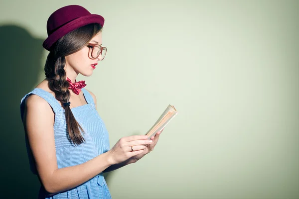 Elegante chica bonita con un sombrero rojo y gafas leyendo un libro — Foto de Stock