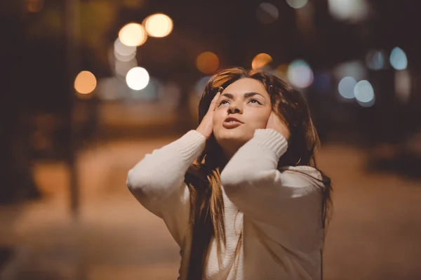Young emotional woman looking up, city street in the night, evening lights bokeh background outdoors — Stock Photo, Image