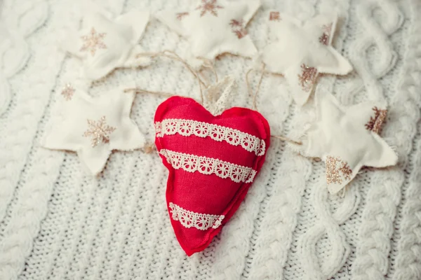 Imagem de close-up de coração vermelho artesanal em fundo de malha cercado por estrelas decorativas — Fotografia de Stock