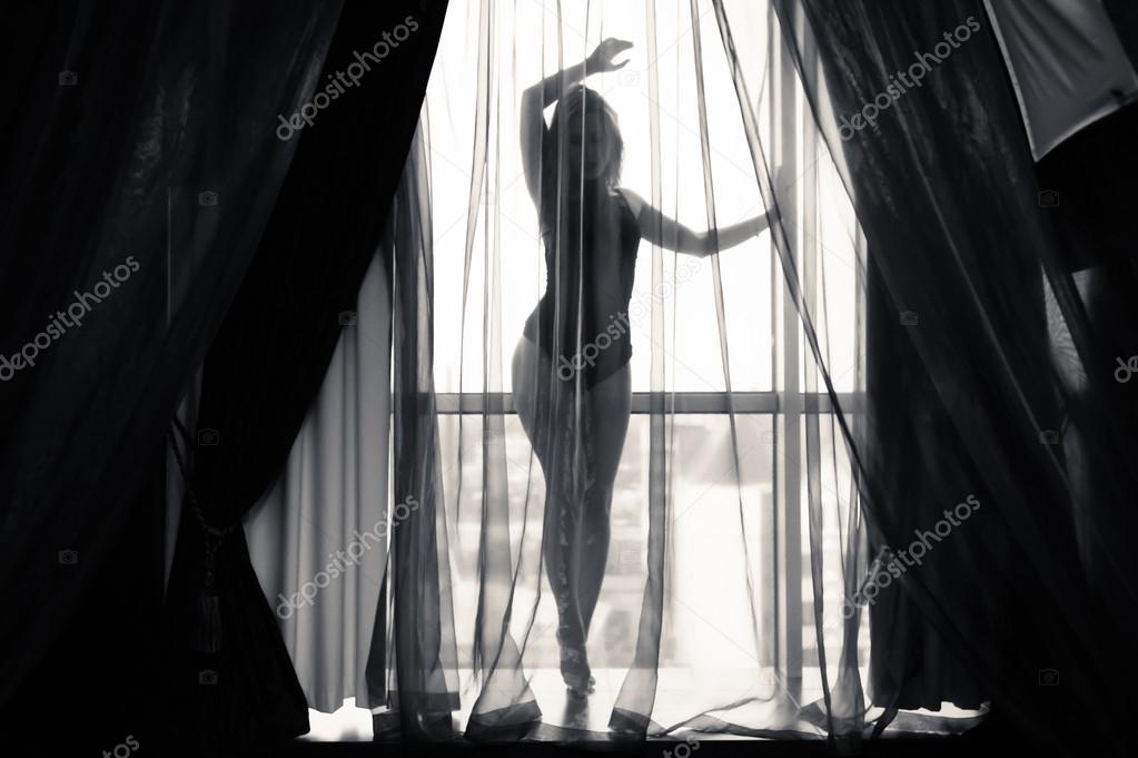 Black and white portrait of sexy beautiful young lady relaxing over light window background