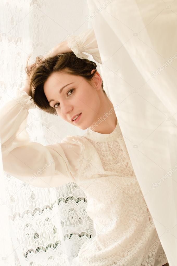 Young lady in white dress at tulle curtain