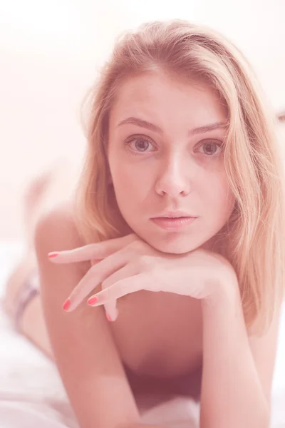 Close up on sensually looking at camera naturally blond young pretty lady with silk skin, excellent hair & red nails having fun relaxing laying in bed on light copy space background portrait image — Stock Photo, Image
