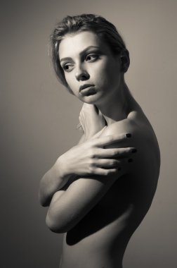 Beautiful young lady looking aside covering her naked shoulder standing posing on copy space background, black and white portrait