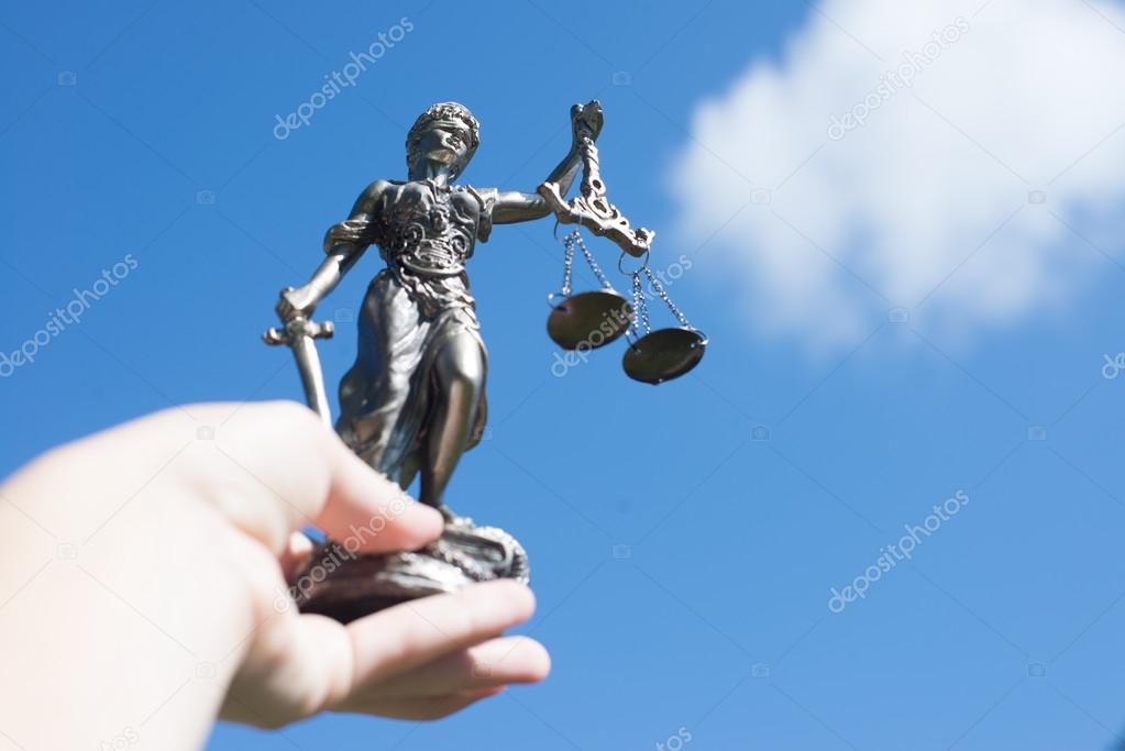 hand holding sculpture of themis, femida or justice goddess up in bright blue sky outdoors copyspace background