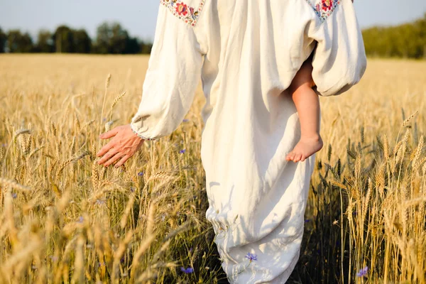 Donna in vestiti etnici che tiene il bambino che cammina attraverso il campo di grano — Foto Stock