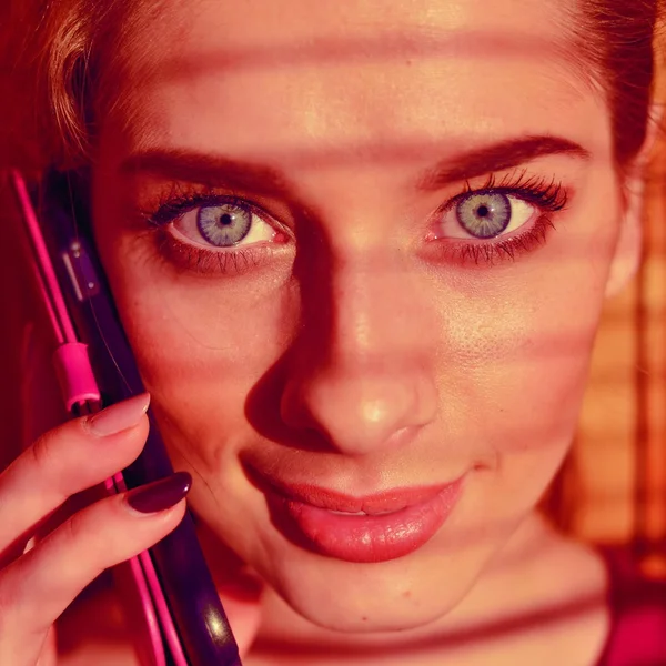 Portrait close up of beautiful young lady talking on mobile phone with shadow from window blinds — Stock Photo, Image