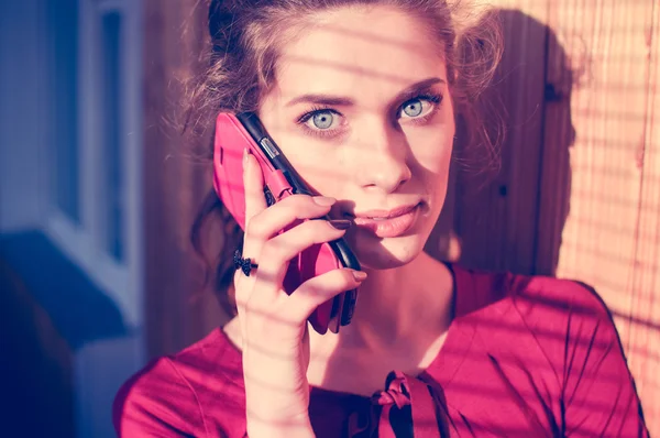 Beautiful young woman talking on mobile cell phone with shadow from window blinds, closeup portrait — Stock Photo, Image