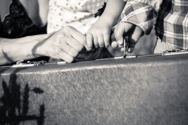 Mothers and two kids hands holding a handle of retro suitcase
