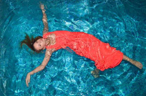 Young pretty lady in red with spread arms and legs in pool — Stockfoto