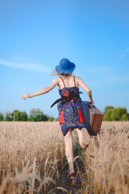 Pretty lady in sundress and bowler hat running away with suitcase