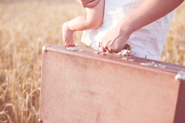 Mano de los padres sosteniendo una maleta retro y un niño pequeño parado en la maleta — Foto de Stock