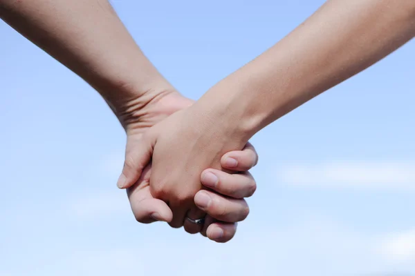 Male and female holding hands outdoors over a blue sky background — 图库照片