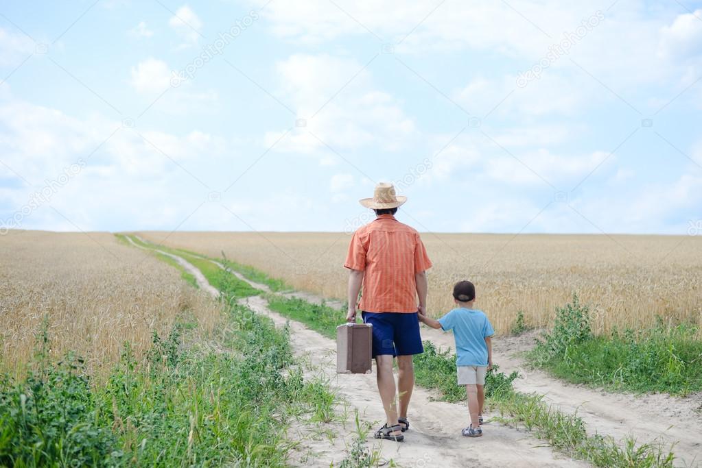 Dad with suitcase holding his son by hand walking away 