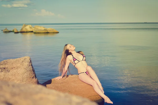 Sexi loira fêmea tomando banho de sol na rocha por mar — Fotografia de Stock