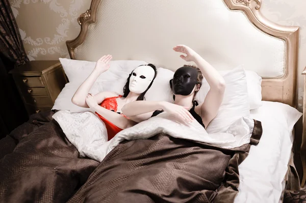 Retrato de bonecas jovens bonitas sexy em máscaras de carnaval se divertindo relaxando na cama — Fotografia de Stock