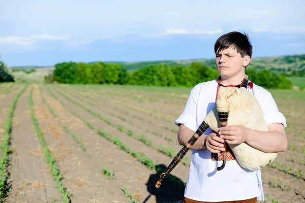 Obrázek muže těší hrát potrubí v ukrajinské tradiční košili na zelené přírodě kopie prostoru letní pole — Stock fotografie