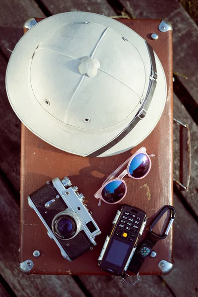Travel background with pith helmet, camera, sunglasses and cellphone on top of retro suitcase — Stockfoto
