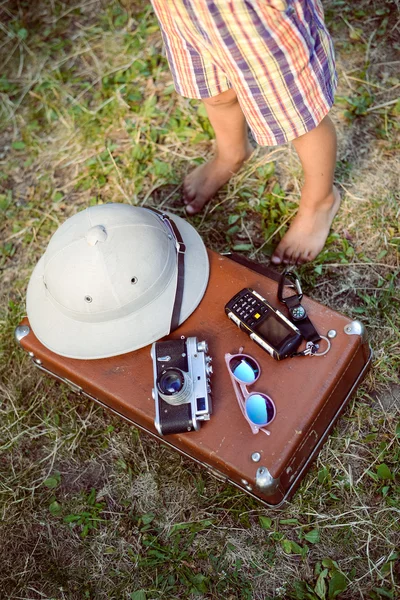 Curious barefoot kid standing by suitcase with travel objects — Stockfoto