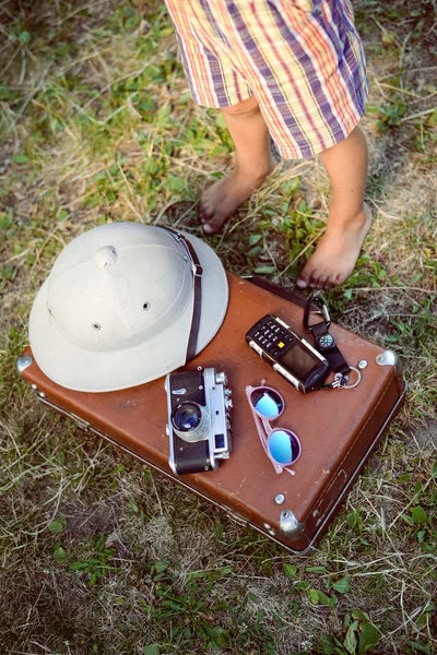 Curious barefoot kid standing by suitcase with travel objects — Zdjęcie stockowe