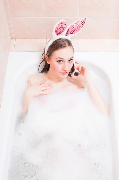 Image de porter des oreilles de lapin drôles et de parler sur un téléphone mobile belle blonde drôle jeune femme sexy regardant la caméra sur l'eau savon espace de copie arrière-plan — Photo