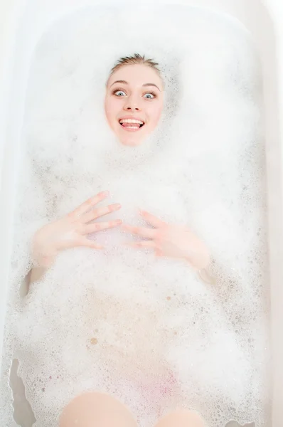 Schöne junge blonde Dame, die Spaß dabei hat, im Seifenwasser zu liegen, sinnlich Zunge zeigt und auf hellem Kopierraum-Hintergrund in die Kamera schaut — Stockfoto
