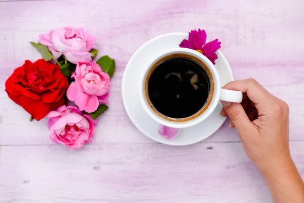 Hand holding cup of coffee with flower petals beside — 스톡 사진