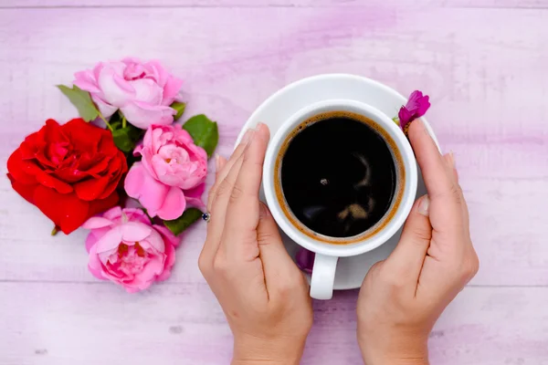 Two hands embracing cup of coffee with flower petals beside — 스톡 사진