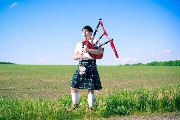 Porträt eines Mannes, der es genießt, Pfeifen im traditionellen schottischen Kilt auf grünen Flächen zu spielen — Stockfoto