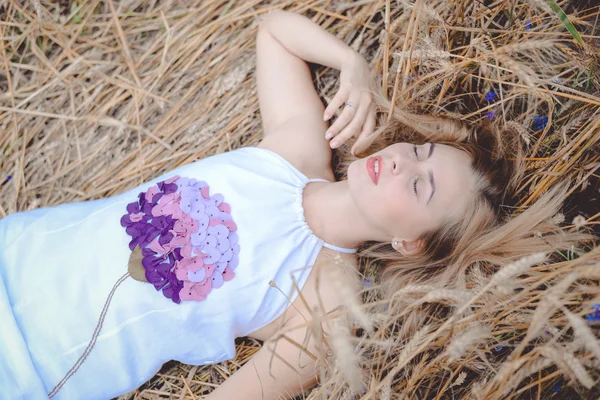 Foto de la señora bonita rubia de pelo largo en vestido largo blanco con decoración de flores en él acostado sobre el heno — Foto de Stock