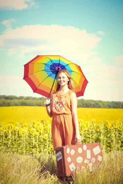 Imagem de bonito feminino segurando guarda-chuva arco-íris e mala de viagem no campo de girassol ao ar livre copiar fundo espaço — Fotografia de Stock