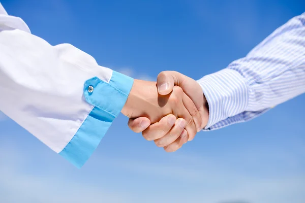 Closeup picture of handshake between a man and a doctor over blue sky sunny outdoors background — Stock Photo, Image