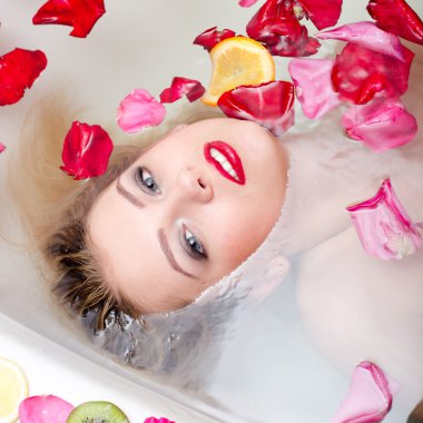 luxury spa queen: elegant blue eyes pinup girl with silk skin having fun laying in water bath and looking at camera relaxing on colorful copy space background, close up portrait