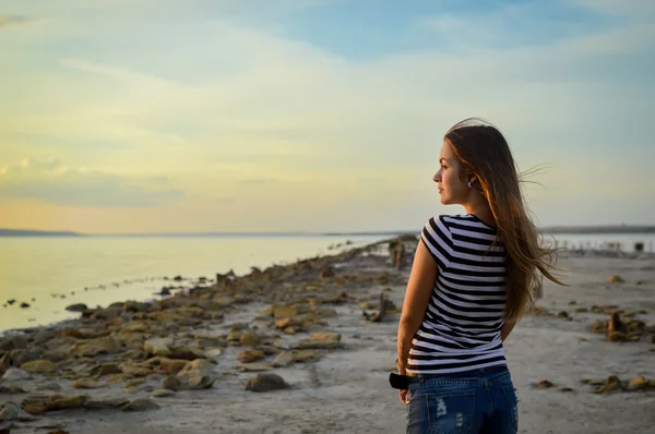 Young woman in striped T-shirt standing on rocky beach — Stock Photo, Image