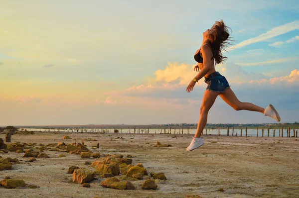 Young sporty lady in shorts and trainers jogging on rocky beach outdoors background copy space — ストック写真