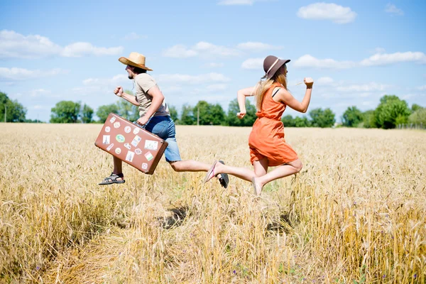 Man with retro suitcase and woman running in opposite sides in field — Stockfoto