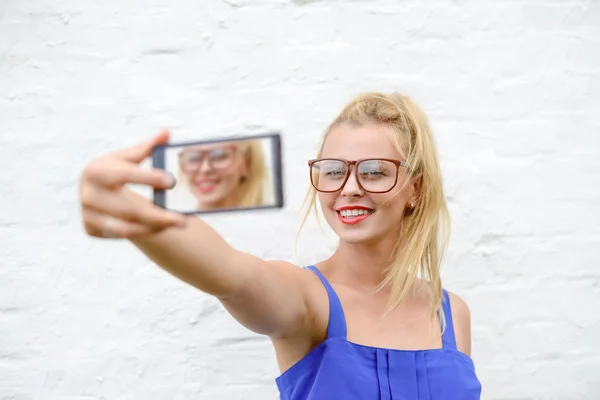 Young happy blond hipster in glasses and blue dress making selfie — Stock Photo, Image