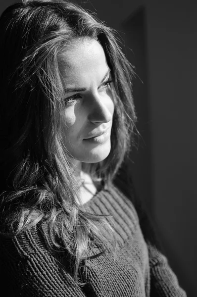Beautiful young woman in woolen sweater enjoying sunshine and looking out the window. Black and white closeup portrait — Stock Fotó