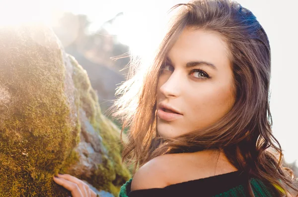 Brunette girl with long hair near moss rocks in backlight