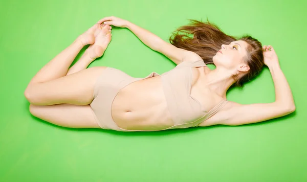 Full length of brunette stretching girl lying on green background — Φωτογραφία Αρχείου