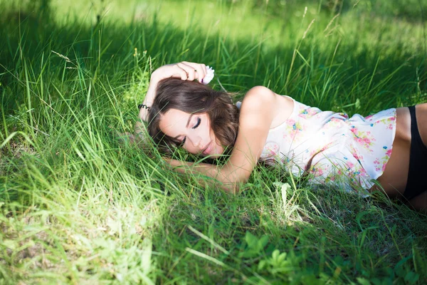 Брюнетка красивая девушка в цветочном топе скользит по длинной зеленой траве — стоковое фото