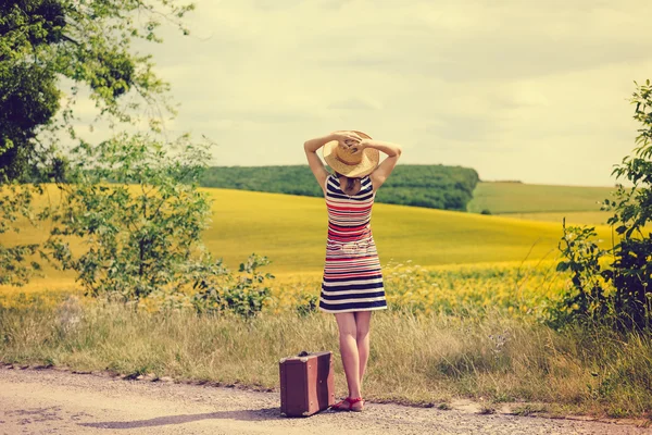 Woman wearing straw hat standing on roadside near yellow field — Stock fotografie