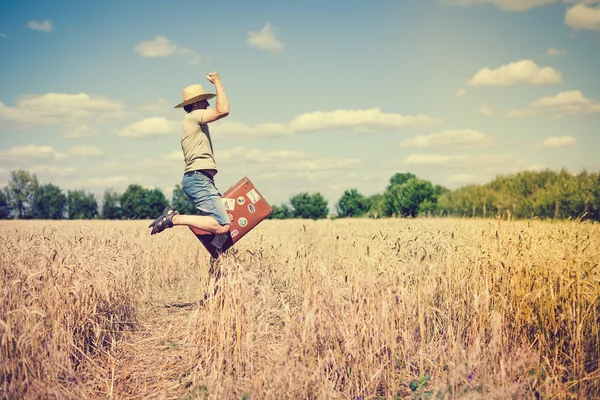Saltando homem usando chapéu de palha com mala no campo de trigo — Fotografia de Stock