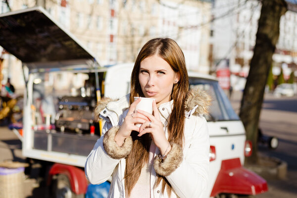 Girl wearing coat holding cup with drink near street food.