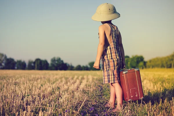 Little boy wearing plaid romper and pith helmet carrying big suitcase in countryside — ストック写真