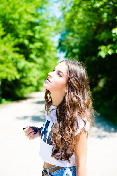 Portrait of brunette girl looking up on road between trees — Stockfoto