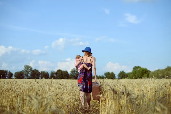 Woman wearing hat with baby-girl walking away on wheat field — 图库照片