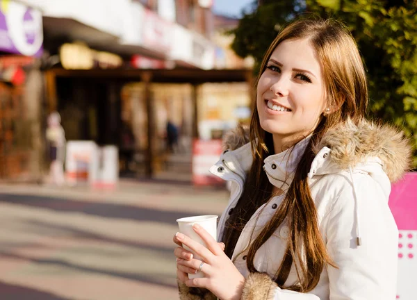 Picture of pretty girl wearing coat holding cup and smiling on street — ストック写真