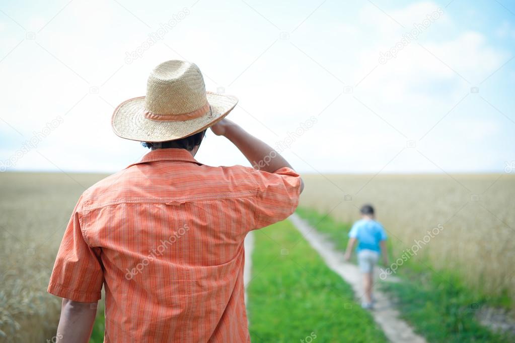 Man wearing straw hat looking after little boy walking away