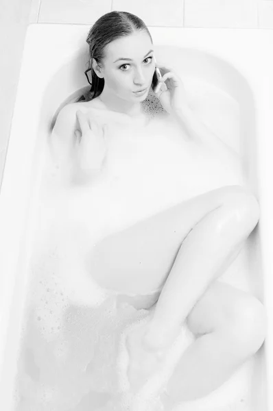 Beautiful sexy young lady having fun happy talking on mobile phone and relaxing in spa bath on soap water copy space background. Black and white picture — Stock fotografie
