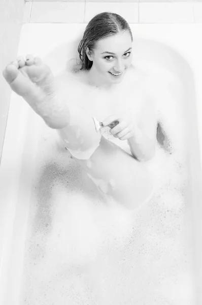 Shaving leg beautiful blond young sensual female having fun happy smiling relaxing and enjoying laying in spa bath on foam water — Stockfoto